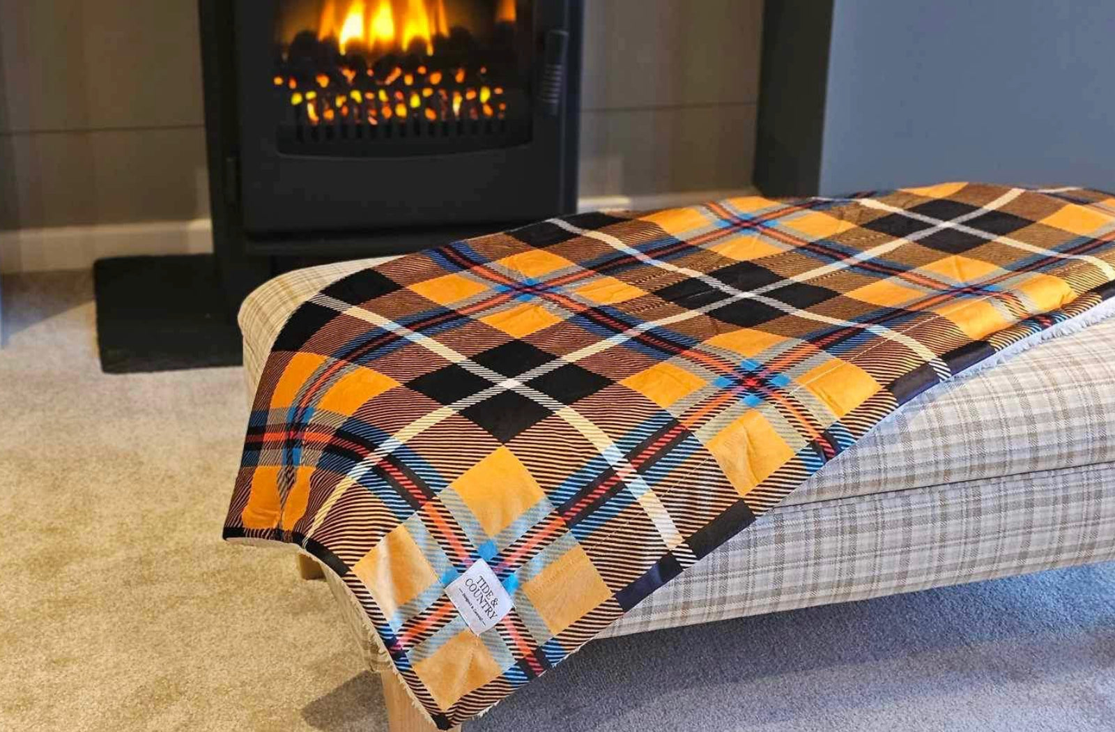 Yellow Cornish Tartan Dog Blanket on a cream footstool by a fireplace