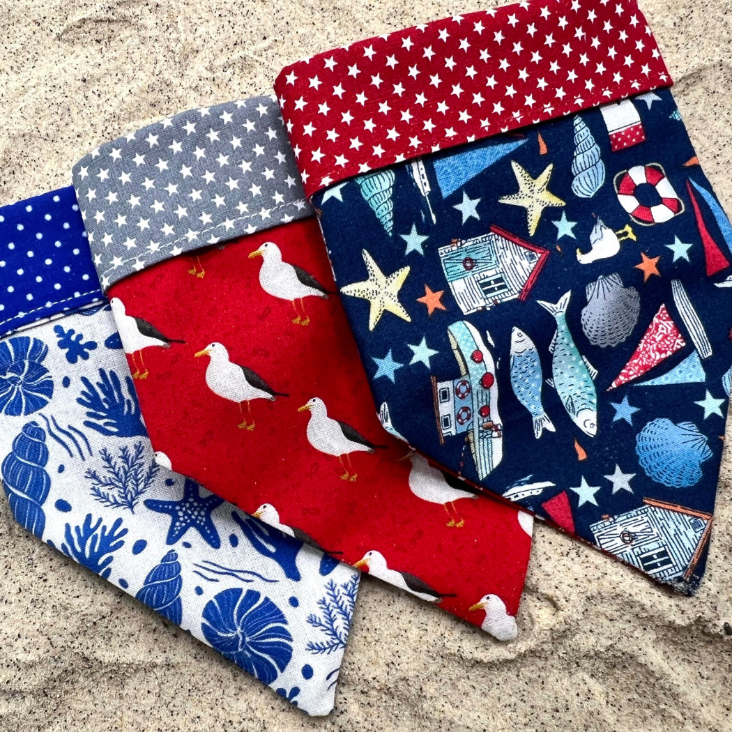 Set of three nautical dog bandanas layed out on sand